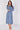 A woman modeling a long-sleeved midi dress with a blue and white paisley pattern, standing against a plain light gray studio background.