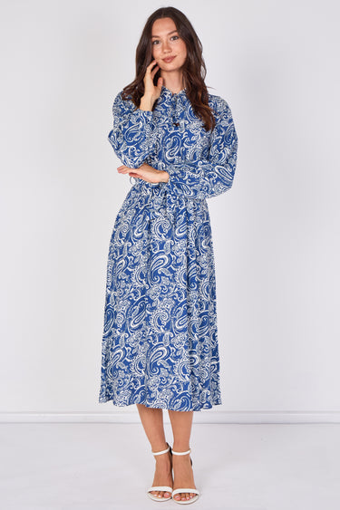 A woman modeling a long-sleeved midi dress with a blue and white paisley pattern, standing against a plain light gray studio background.