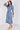 A woman modeling a long-sleeve midi dress with a blue and white paisley pattern, standing against a light gray studio background.
